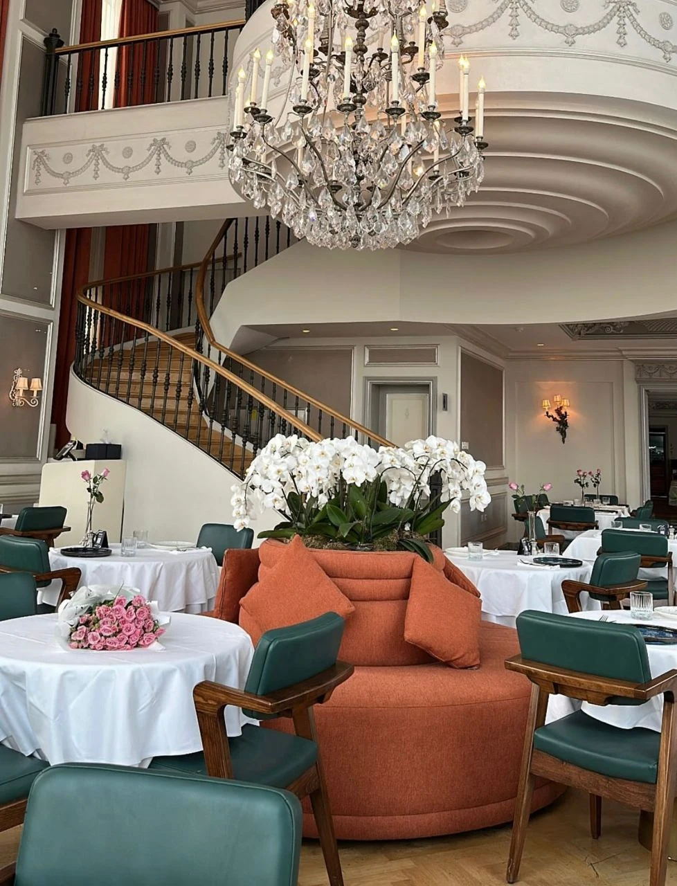 Restaurant interior with upholstered seating, a curved staircase and chandelier